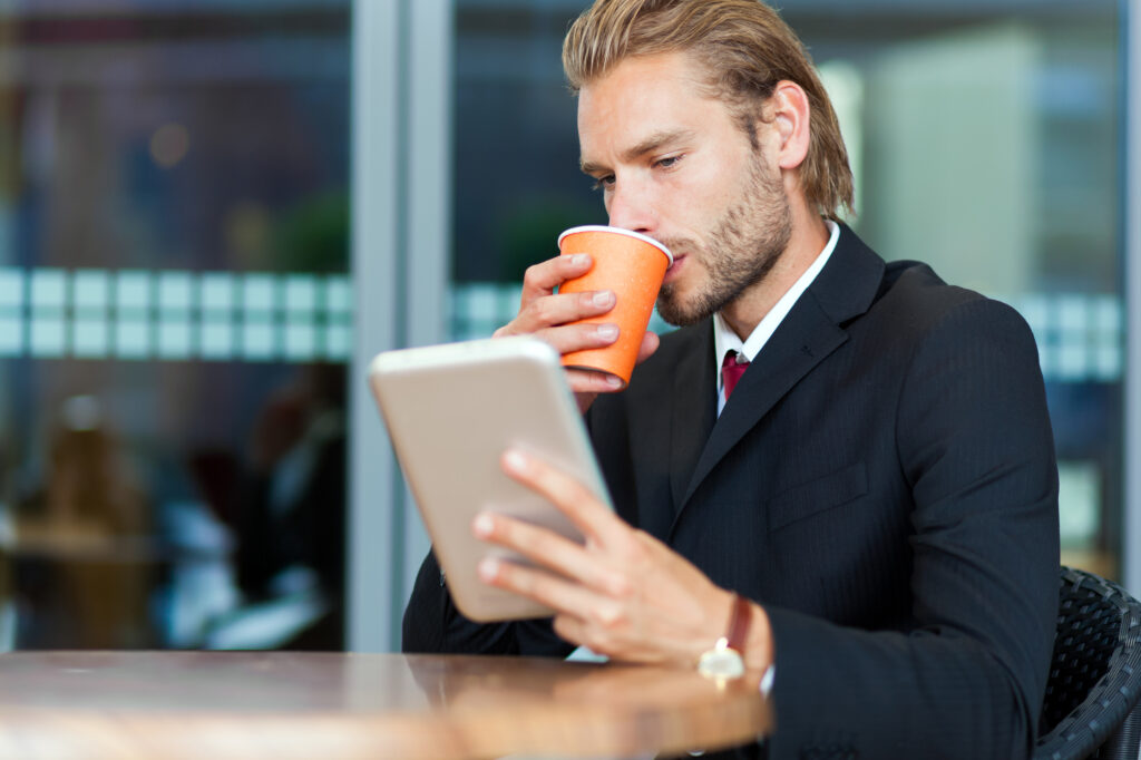 man sipping coffee while looking at his tablet