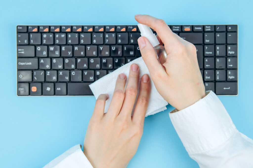 person cleaning their keyboard with a spray bottle and wipe