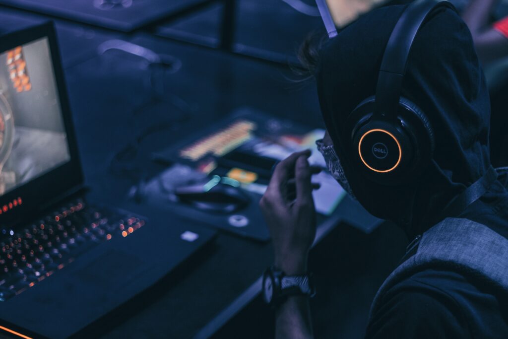 person wearing headphones gaming on laptop in dark room