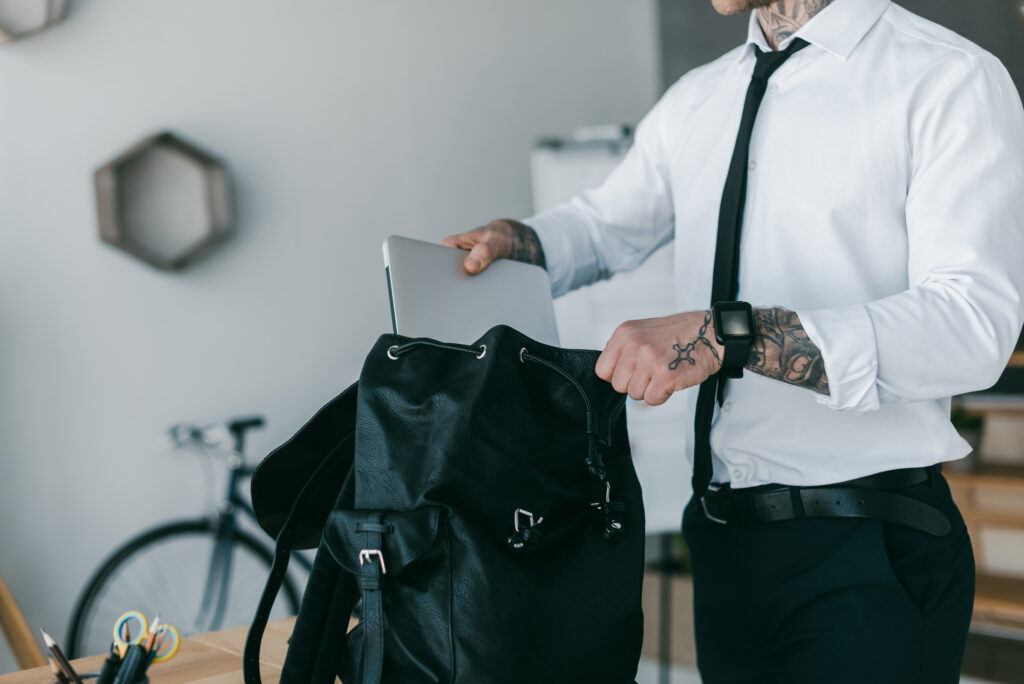 man in dress shirt and tie putting laptop into a black backpack