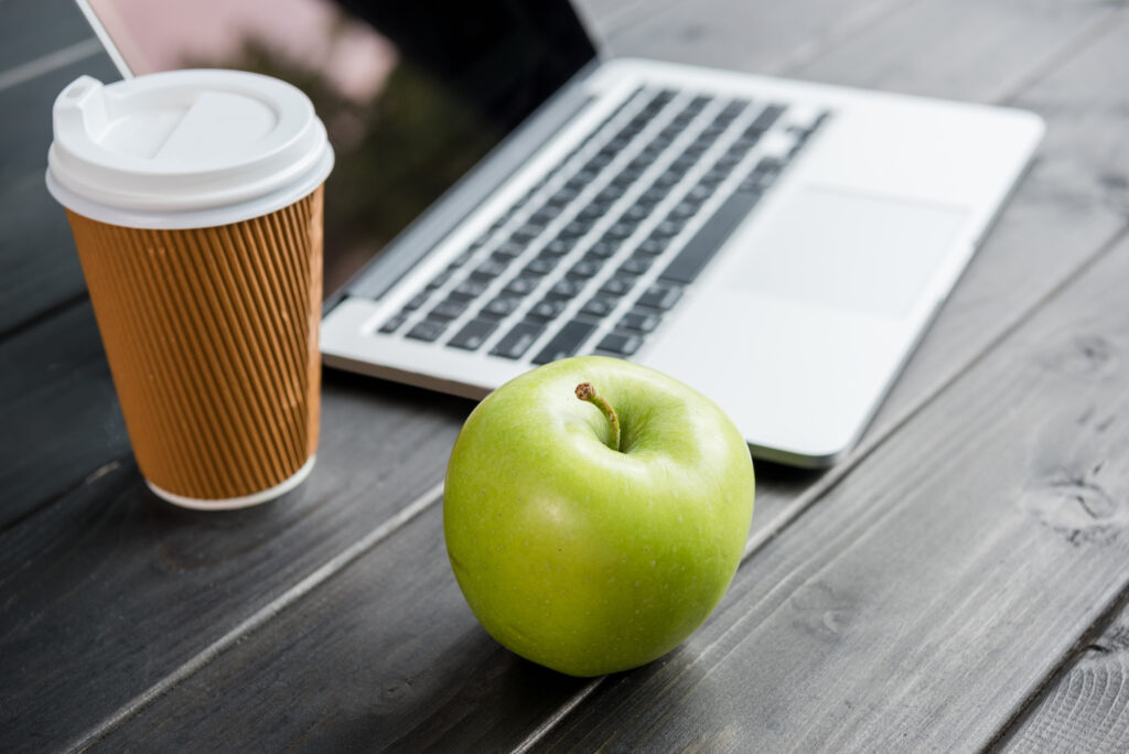 laptop sitting on table next to coffee cup and a green apple