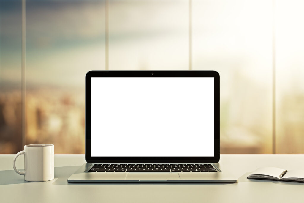 laptop with blank screen sitting on table top with a notebook and cup of coffee