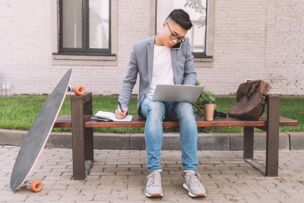 person sitting on bench with laptop and longboard, working on the go