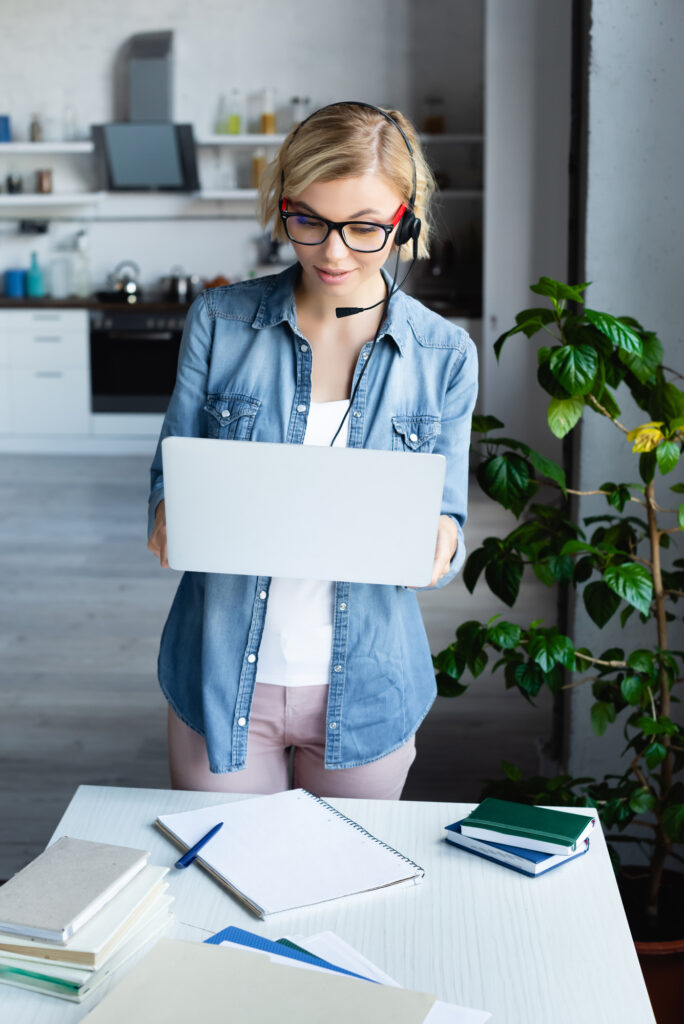woman with headset on standing and holding laptop while she works