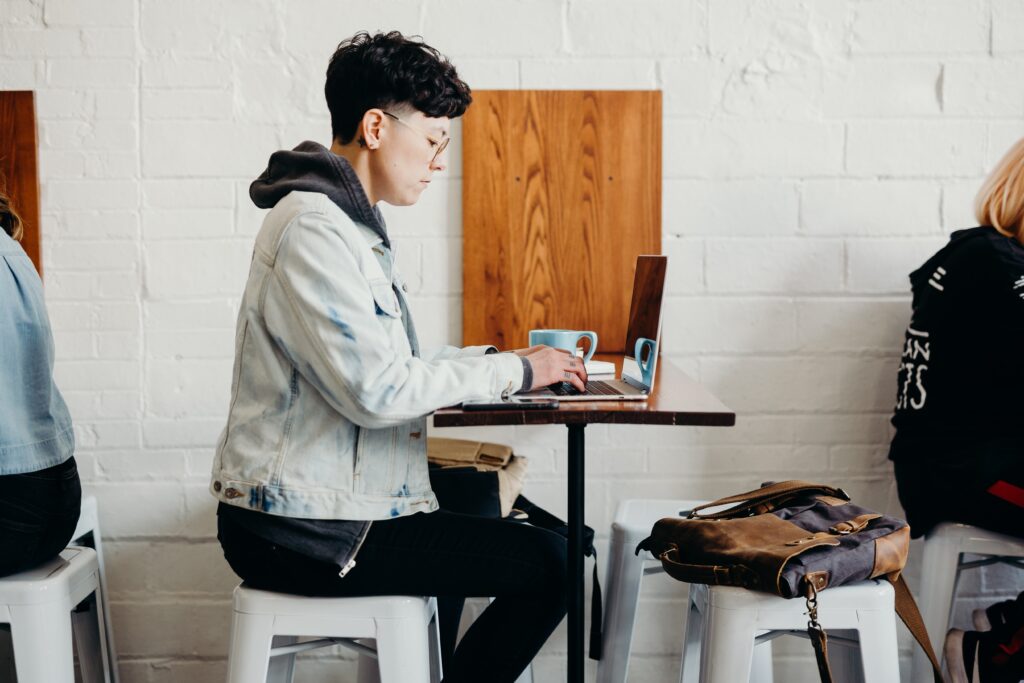 person sitting at desk working on laptop with laptop backpack sitting on floor next to them.