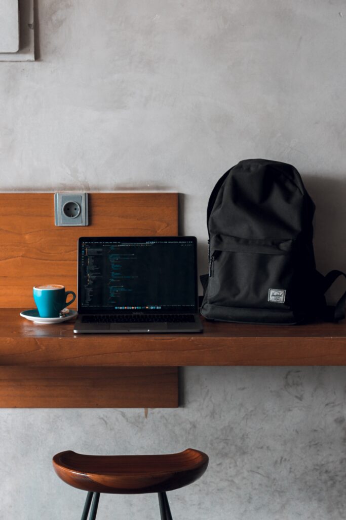 laptop sitting on desk next to laptop backpack and cup of coffee