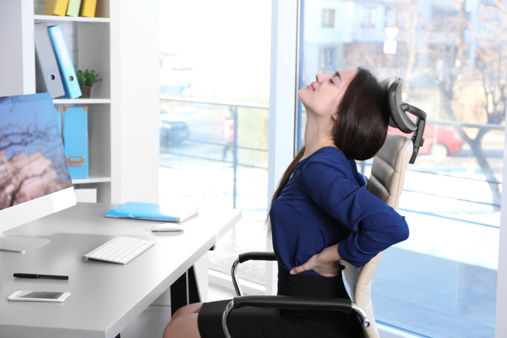 Posture concept. Young woman suffering from back pain while working with computer at office