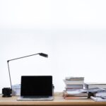 laptop sitting on desk with lamp and stack of books