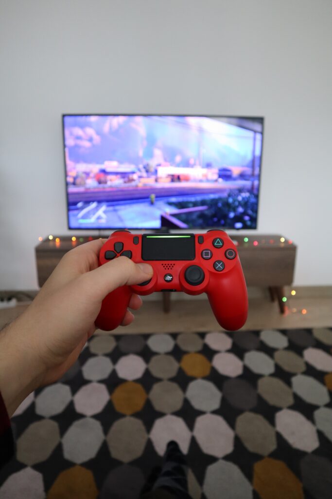 person holding a red gaming controller in front of large monitor