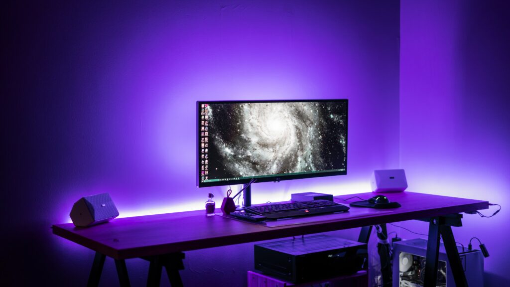 Widescreen desktop monitor sitting on desk with a purple backlight