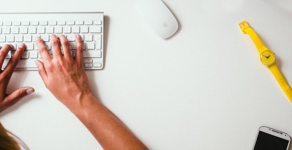 person typing on a computer with yellow watch sitting on desk next to them