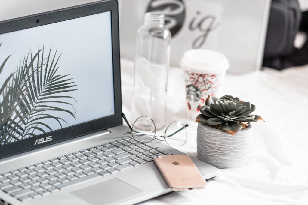 Asus laptop sitting on white desk next to smartphone and glasses