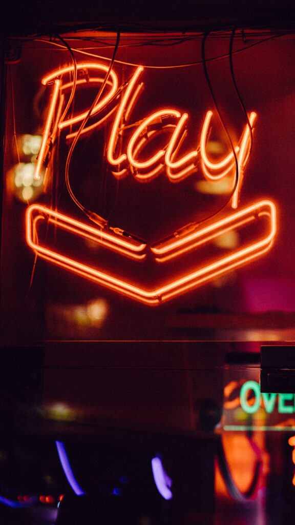 Neon sign that reads "Play" on outside of arcade bar