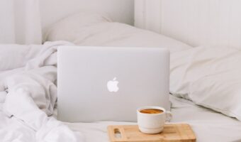laptop sitting on white bed next to cofee mug