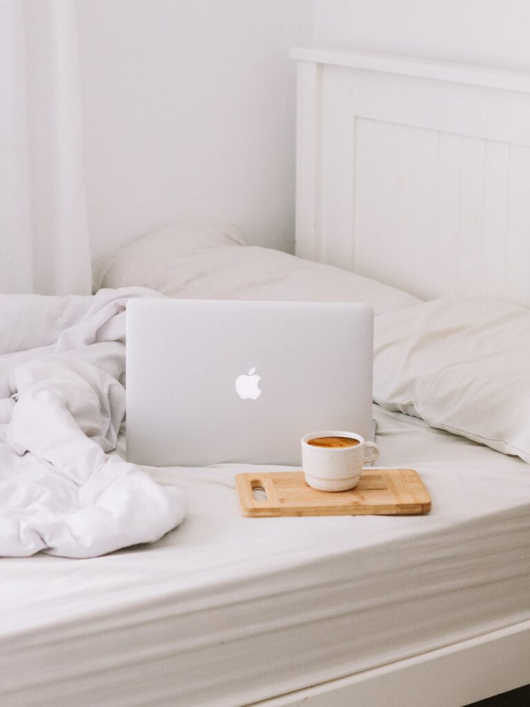 laptop sitting on white bed next to cofee mug
