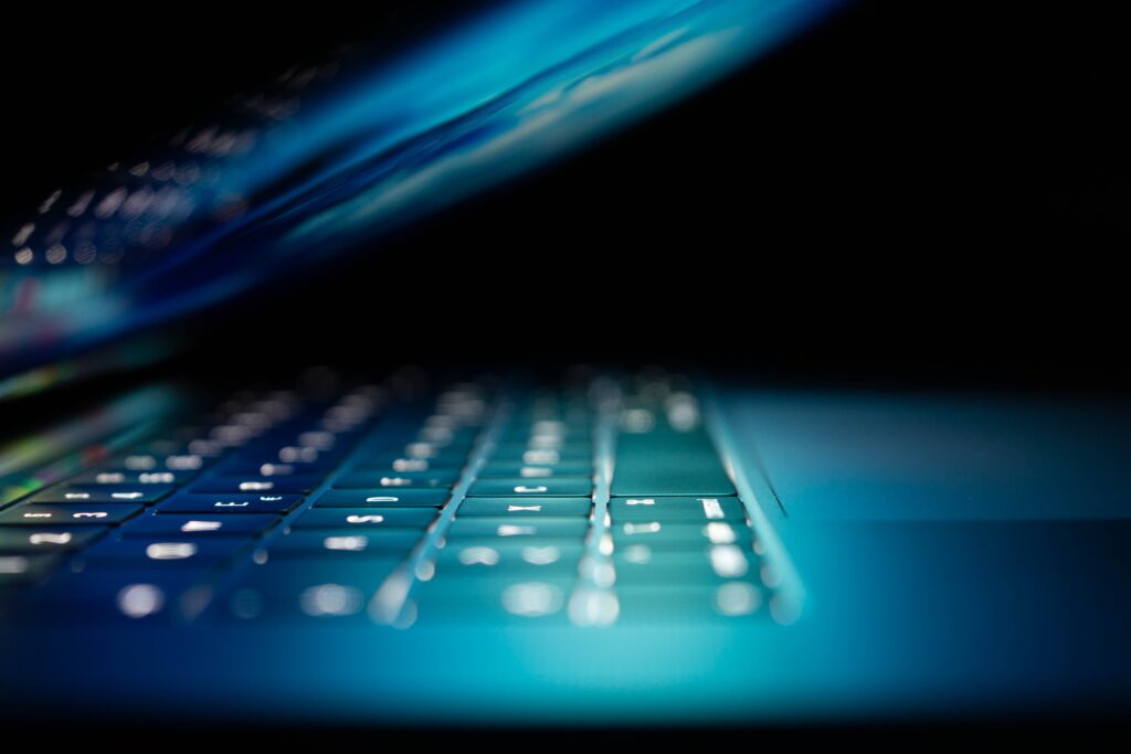 Laptop in dark room open halfway showing blue backlit screen