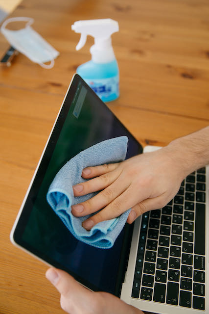 Hand holding microfiber towel wiping down laptop screen with LCD screen cleaner