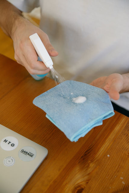 Hand spraying solution on blue microfiber towel about to wipe down laptop screen