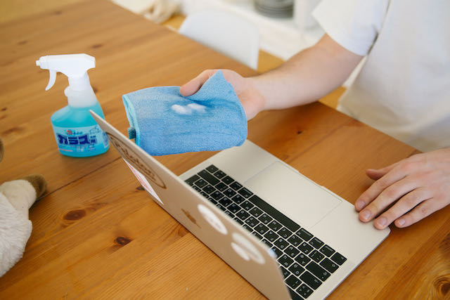 Hand holding blue microfiber towel with cleaning solution on it about to wipe down a laptop screen